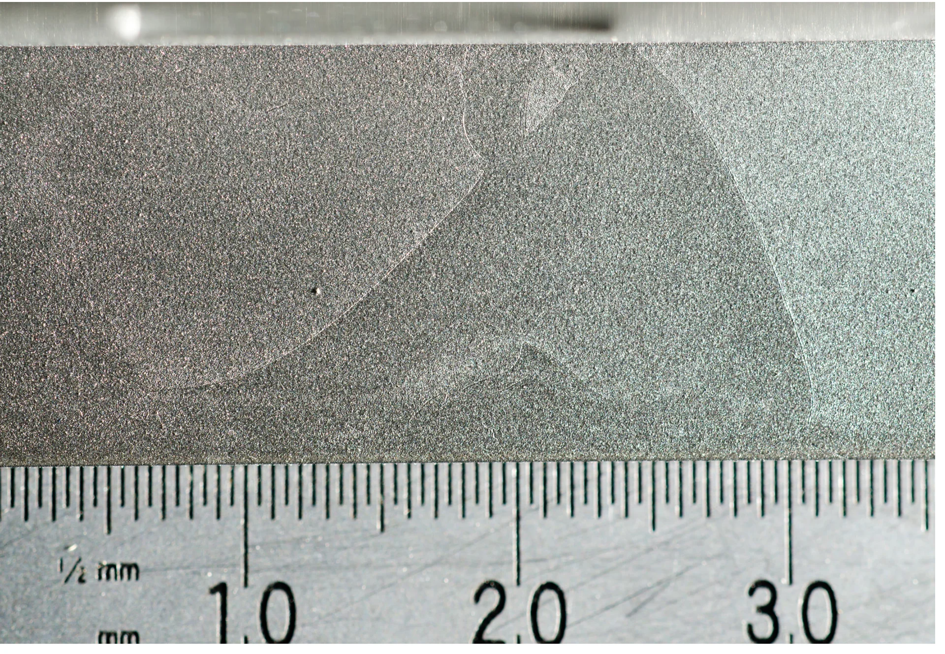 Surface-detail photograph with a scale, from the October 2014 temporary cosmetic-deviation document. This crop shows the defect being discussed; it does not establish the final acceptance limit or a production-yield result.
